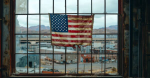 An aging U.S. flag hangs in a shuttered industrial window — a quiet reminder of the nation's once-thriving manufacturing base.
