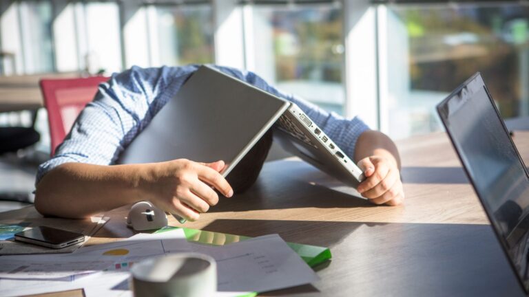 Man looking fed up with his head underneath his Windows 11 laptop