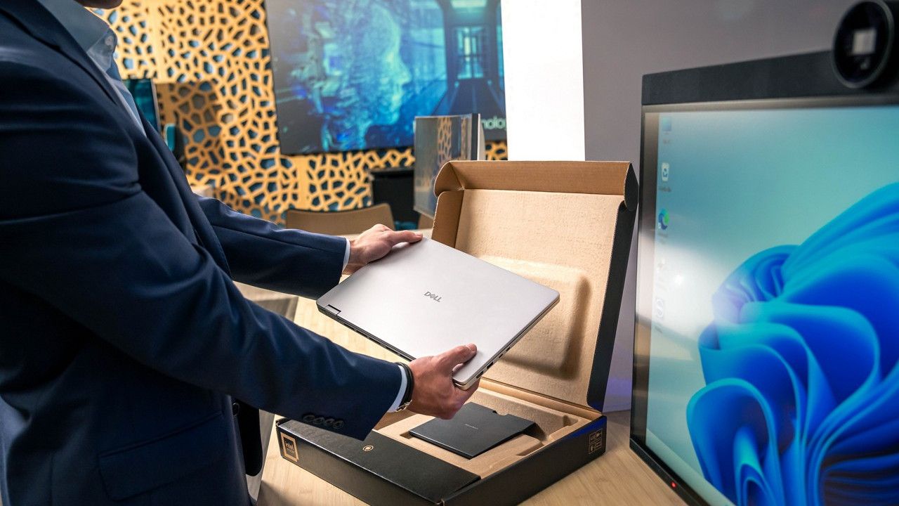 Dell laptop being removed from its box on a desk next to a monitor