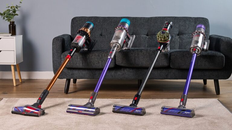 Four Dyson cordless stick vacuums leaning against a sofa