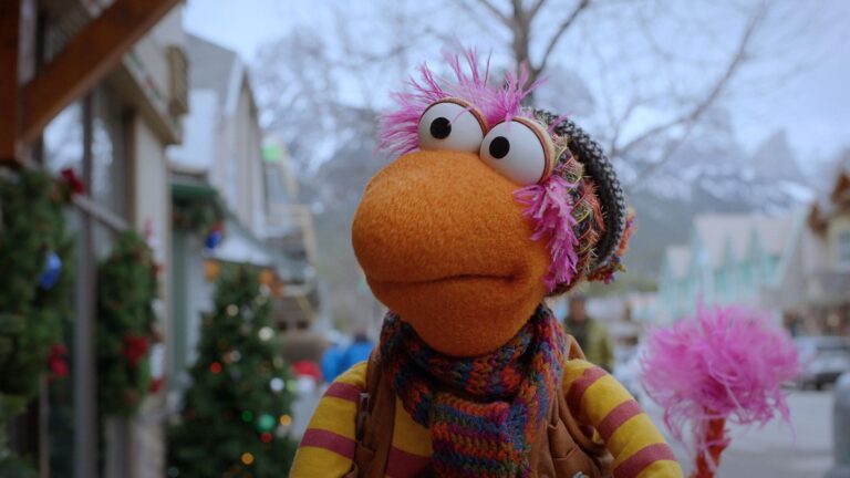 Still from The First Snow of Fraggle Rock showing a puppet wearing a nice warm jumper and scarf in a street with christmas decorations