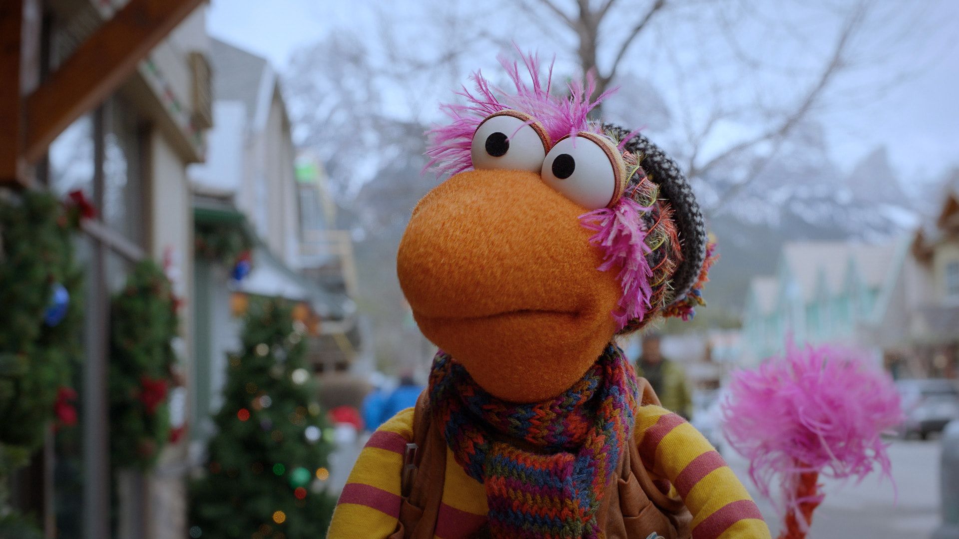 Still from The First Snow of Fraggle Rock showing a puppet wearing a nice warm jumper and scarf in a street with christmas decorations