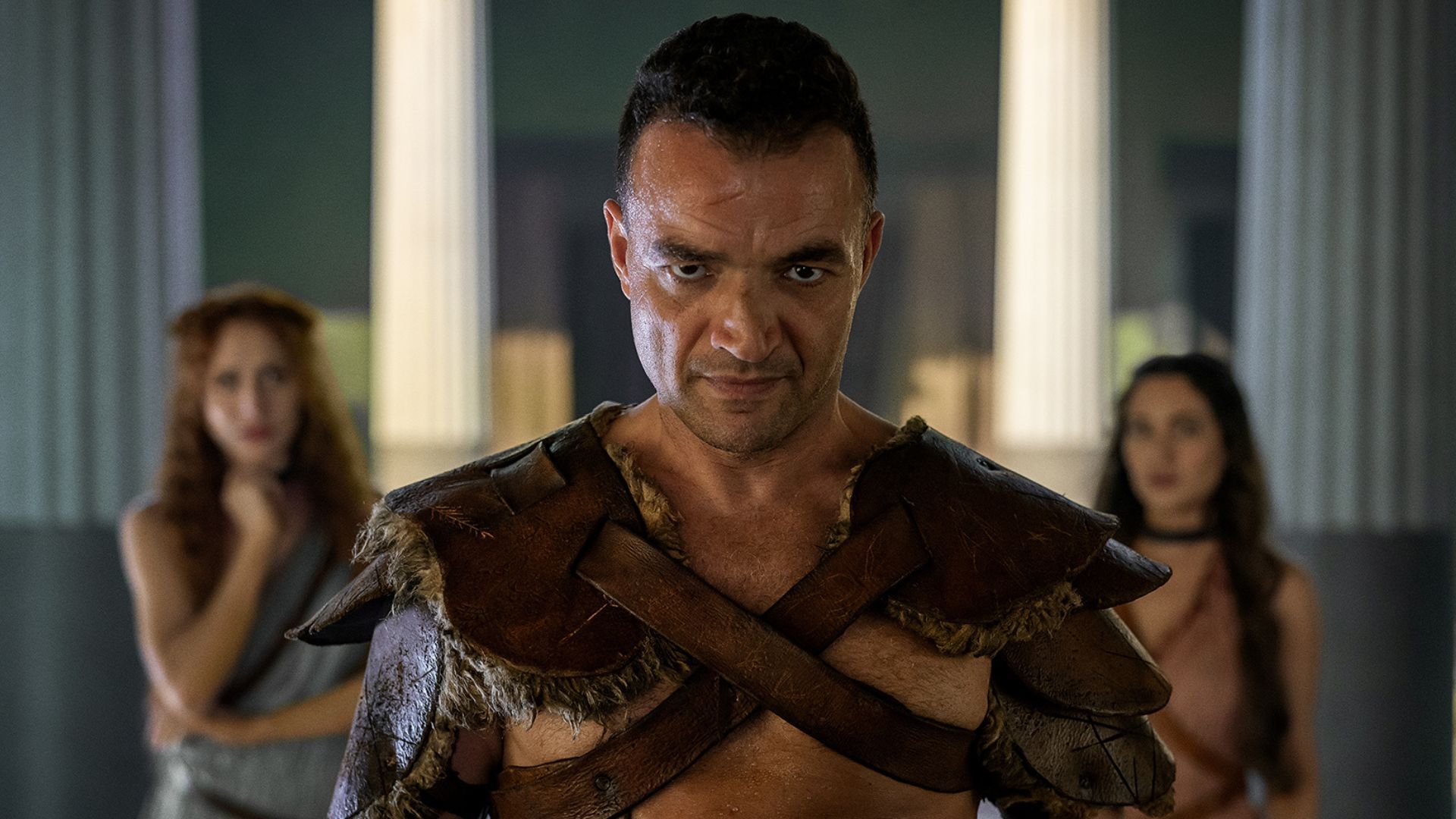 Ashur stands between two women, who are in the background