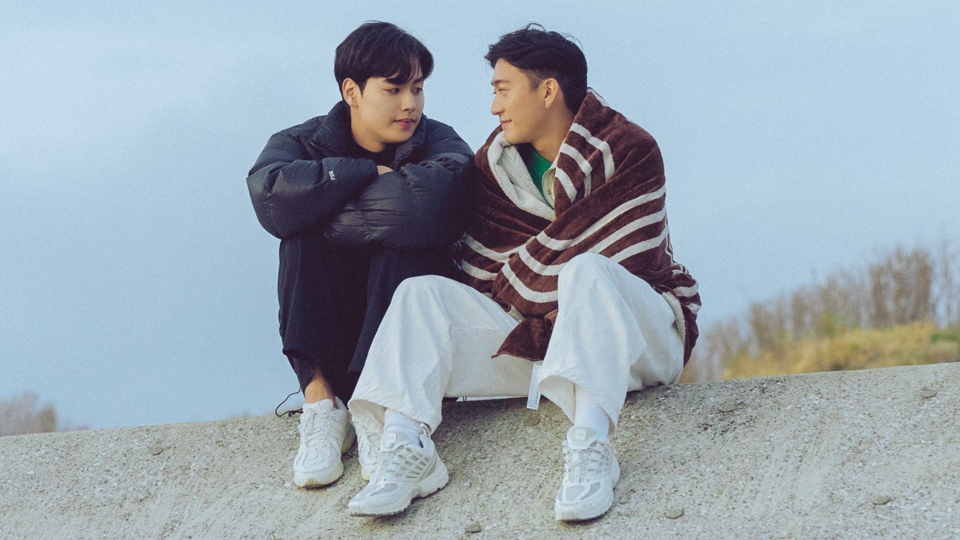 Two guys talk to each other while sitting on a wall