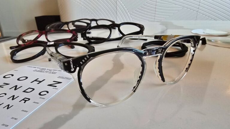 A prototype version of IXI's smart glasses is unpainted to reveal the components hidden within the frame. At back, the finished product.