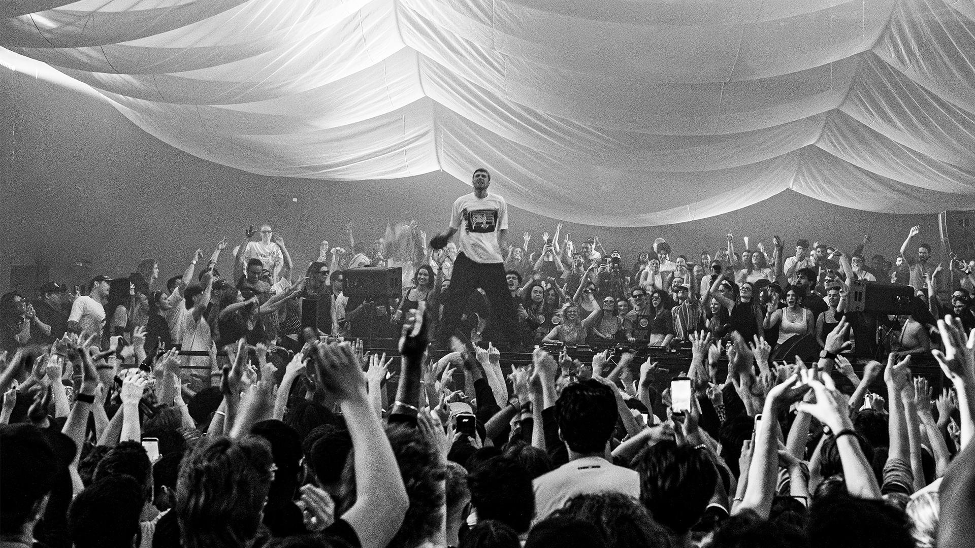 Fred again.. stands in the middle of a crowd during his USB002 gig in Toronto surrounded by people. The photo is in black and white.