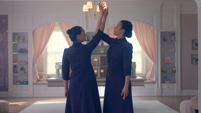 Two girls dressed in plum dance in the middle of a bedroom