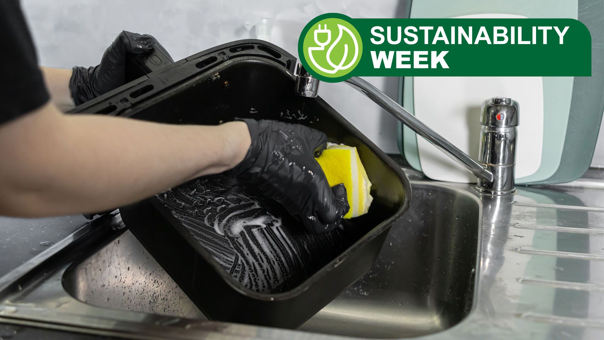 Person wearing black gloves washing air fryer basket in kitchen sink