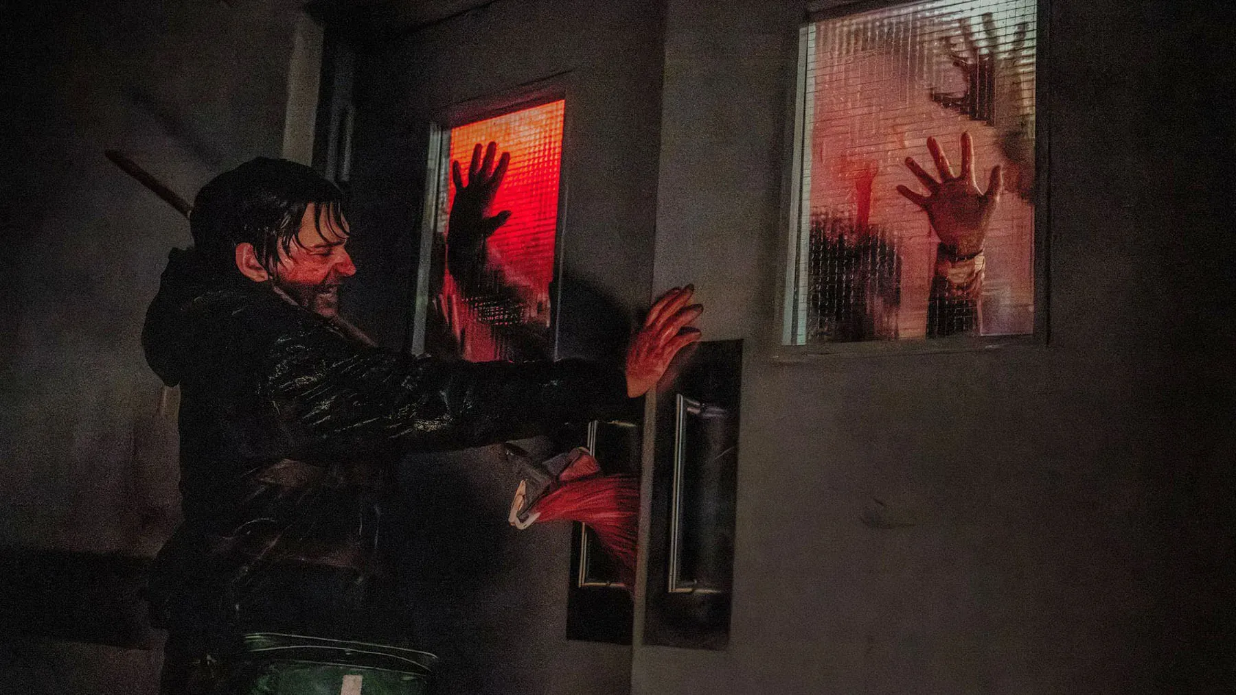 A man barricades himself behind a door while bloodied handprints are visible on the other side
