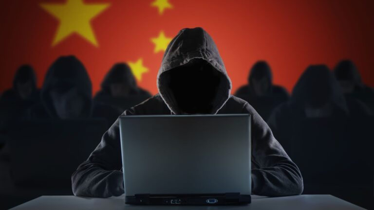 A group of hackers all wearing black with hoods pulled up over their heads with an open laptop in front of them. The background is a Chinese flag