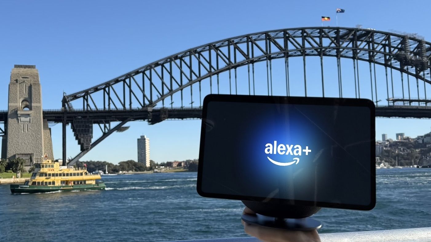 An Amazon Echo smart display with an Alexa Plus graphic posed in front of the Sydney Harbour Bridge