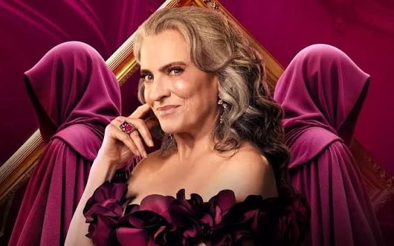 The Traitors Australia season 3 host Gretel Killeen wearing a dark blush read ball gown smiling in foreground, backed by two hooded Traitors 3 contestants in crimson robes