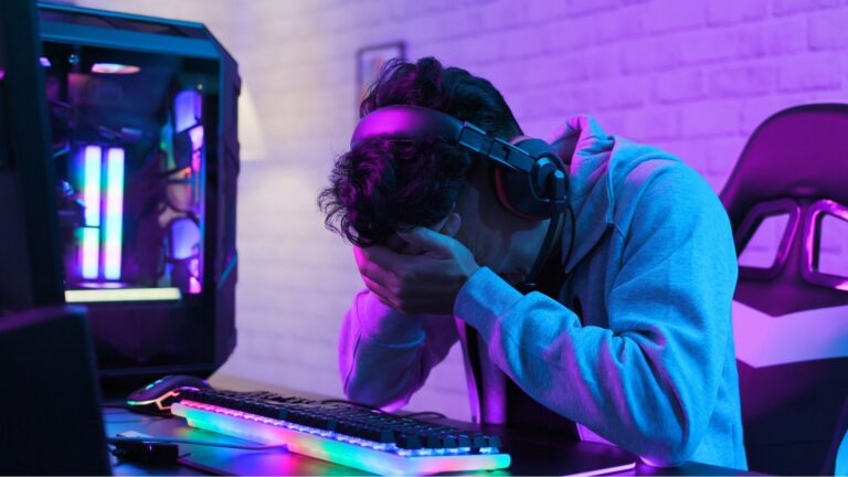 Frustrated PC gamer sat at desk holding head in hands