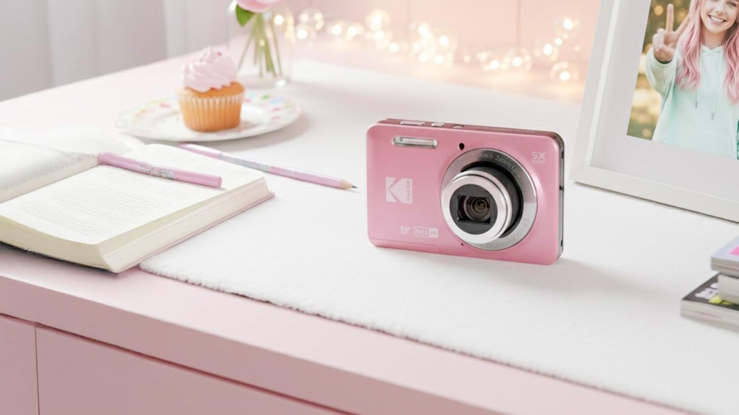 Kodak PixPro FZ55 in pink, on a bedroom desk with pink frontage, notebook, pinks pens, cupcake, picture frame