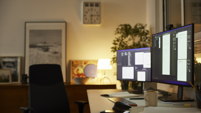 A home office, low lit, with two PCs and monitors on a desk by an empty chair