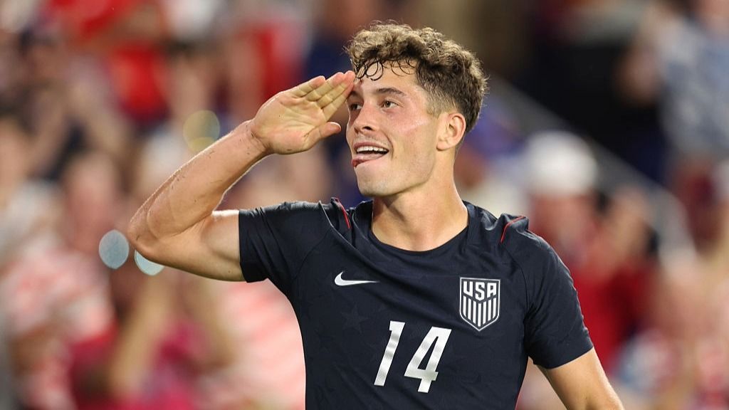 Sebastian Berhalter, wearing the USA national team's black away kit, salutes the fans after scoring in an international friendly.